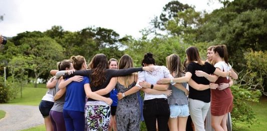 Mulheres se abraçam em uma roda de mais ou menos 20 pessoas, na beira de uma piscina