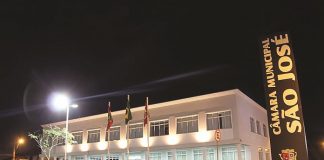 fachada do prédio da câmara vista de lado à noite, bem iluminada, com uma placa à direita escrita Câmara de Vereadores de São José, na vertical