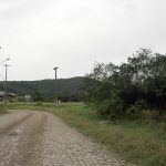 rua de paralelepídeos antiga que faz uma curva à esquerda com um terreno baldio em volta