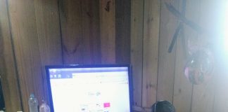 agente de segurança com um colete escrito IGP nas costas sentado em frente à um computador em um barraco de madeira
