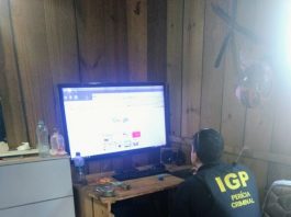 agente de segurança com um colete escrito IGP nas costas sentado em frente à um computador em um barraco de madeira