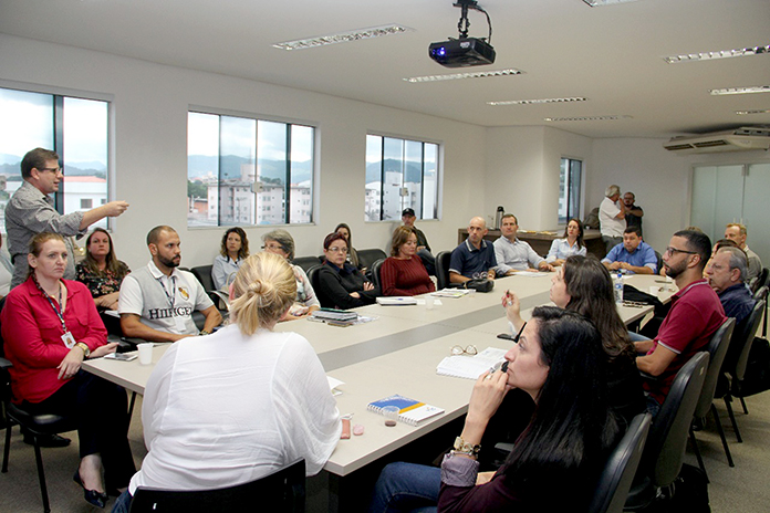 20 pessoas em reunião, entre homens e mulheres, ao redor de uma grande mesa