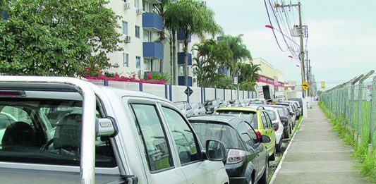 carros estacionados ao longo do meio fio de uma rua com prédios ao fundo