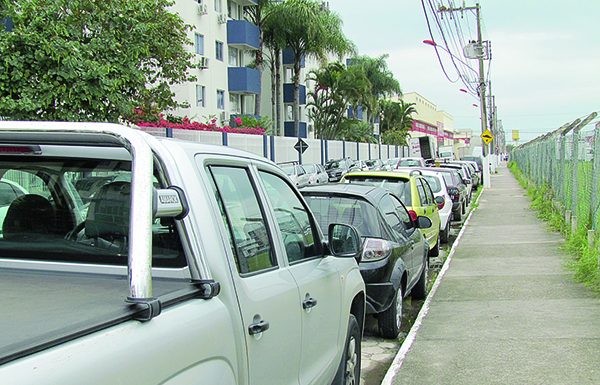 carros estacionados ao longo do meio fio de uma rua com prédios ao fundo