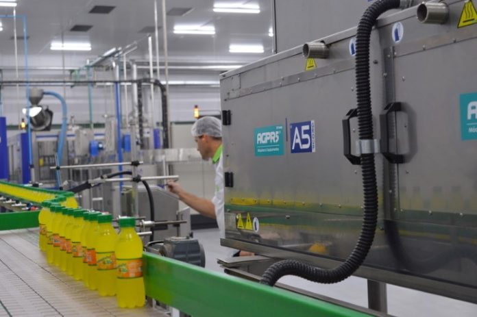 equipamentos de uma fábrica com um funcionário inspecionando garrafas em linha
