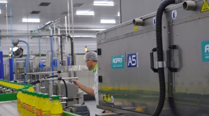 equipamentos de uma fábrica com um funcionário inspecionando garrafas em linha