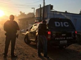 dois agentes da polícia civil vistos de costas a lado de uma caminhonete com grande inscrição no vidro escrita DIC