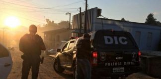 dois agentes da polícia civil vistos de costas a lado de uma caminhonete com grande inscrição no vidro escrita DIC