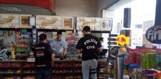 Em loja de conveniência de posto, dois agentes, um do procon e outro da polícia, conversam com funcionário atrás do balcão