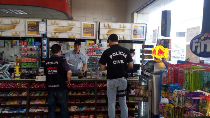 Em loja de conveniência de posto, dois agentes, um do procon e outro da polícia, conversam com funcionário atrás do balcão
