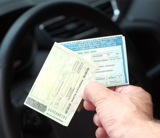 duas carteiras de motoristas seguradas por uma mão com o interior de um carro ao fundo