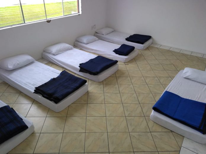 pequena sala com janela e colchões iguais no chão com travesseiros brancos e cobertores azuis