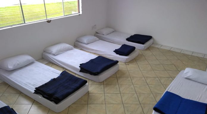 pequena sala com janela e colchões iguais no chão com travesseiros brancos e cobertores azuis