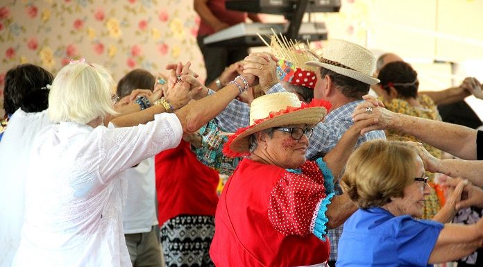 Idosos vestidos com trajes de arraiá fazem um túnel com as mãos em dança coletiva