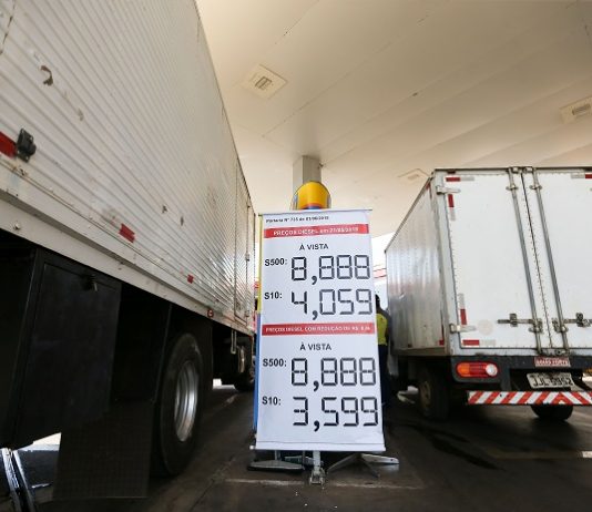 dois caminhões vistos pela parte de trás estacionados lado a lado em um posto com um banner mostrando os preços