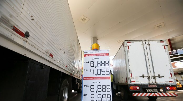 dois caminhões vistos pela parte de trás estacionados lado a lado em um posto com um banner mostrando os preços