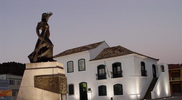 estátua de figura feminina iluminada em uma praça em frente a um casarão histórico