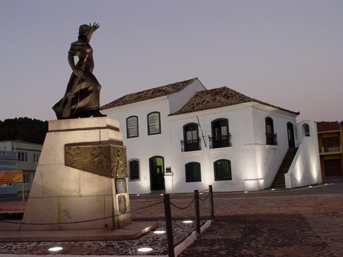 estátua de figura feminina iluminada em uma praça em frente a um casarão histórico