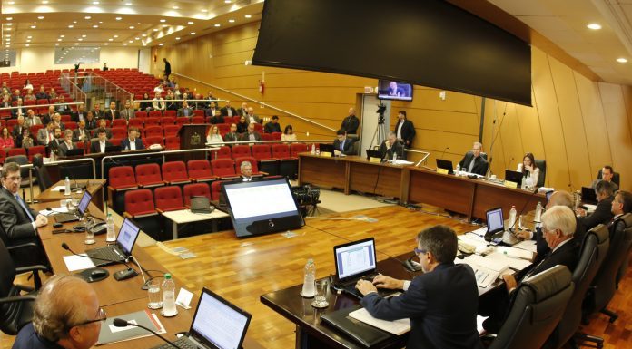 grande auditório com bancada retangular à frente onde sentam os conselheiros com computadores à frente