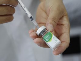 close em nas mãos de uma pessoa extraindo conteúdo de pequeno fraco de vidro com uma seringa