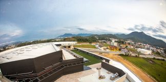 vista aérea de parte do prédio, mostrando um terraço e terreno em baixo, com casas ao fundo da imagem