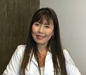 Acupuntura faz a diferença na vida de bebês e crianças mulher de descendência oriental sorri para a câmera, sentada e trajando uma blusa branca