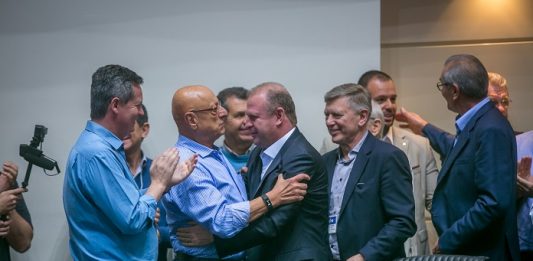 Após lançamento de candidatura, Merisio espera boa notícia amin e merisio se cumprimentam sorridentes ao centro da fotos, com outros homens em volta