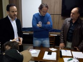 três homens em pé lado a lado em volta de uma mesa em um escritório