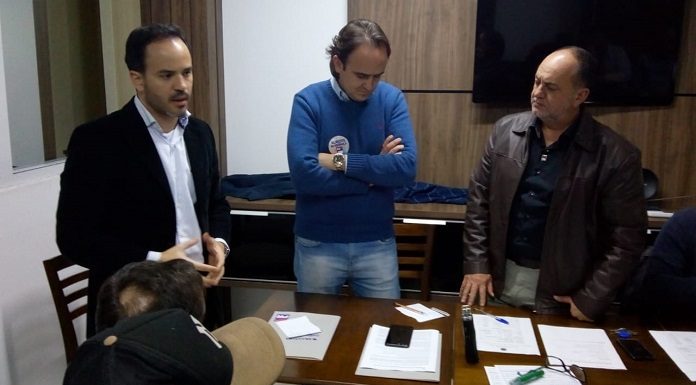 três homens em pé lado a lado em volta de uma mesa em um escritório