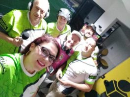 michelle faz selfie com colegas em cabine de transmissão, todos usando o mesmo uniforme verde