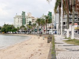Áreas verdes em Coqueiros são asseguradas para o município pequena praia onde há calçada alta, ao lado de rua e prédios ao fundo