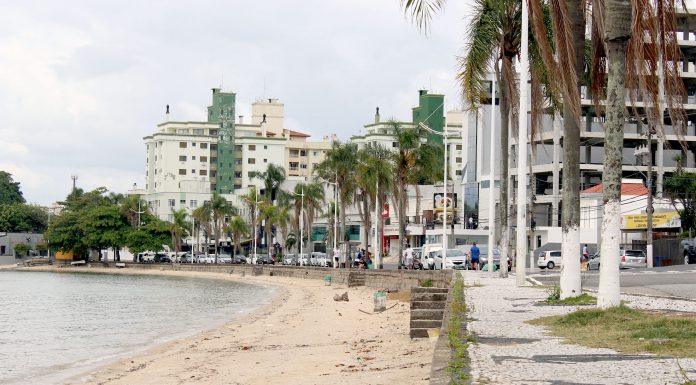 pequena praia onde há calçada alta, ao lado de rua e prédios ao fundo