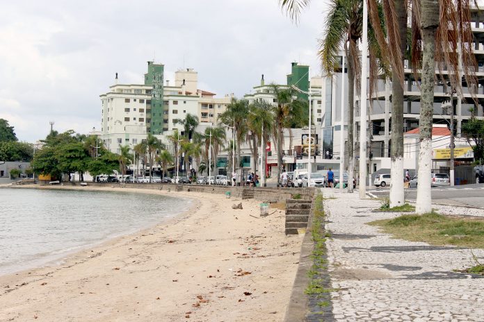 pequena praia onde há calçada alta, ao lado de rua e prédios ao fundo