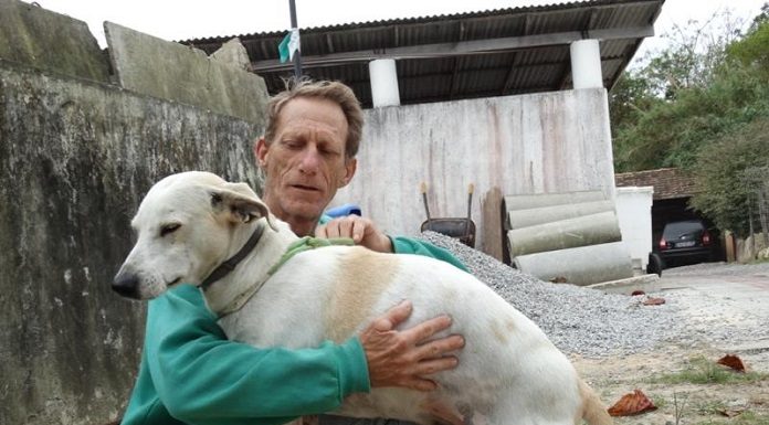 Homem abraça um cão branco de porte médio usando uma coleira