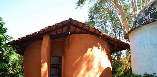 casa com formatos curvos, de cor alaranjada, com algumas plantas em volta