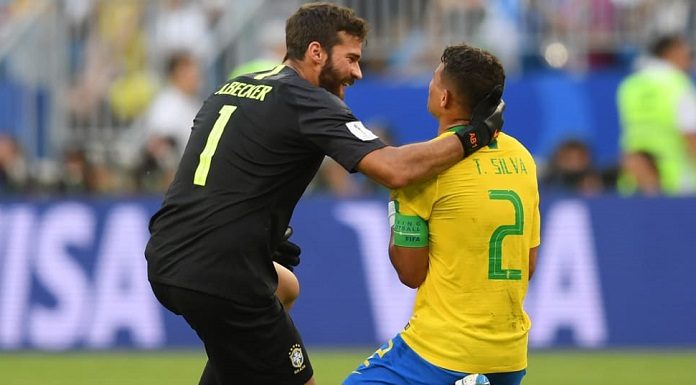 dois jogadores de brasil ajoelhados no gramado; goleiro brasileiro pega na cabeça do zagueiro thiago silva; estão comemorando