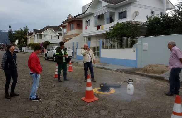 pessoas observam o aparelho fazendo fumaça sobre uma boca de lobo no meio de uma rua