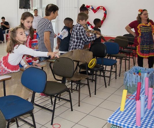 crianças vestidas de jeca brincam de jogar argola em um salão com algumas cadeiras dispostas