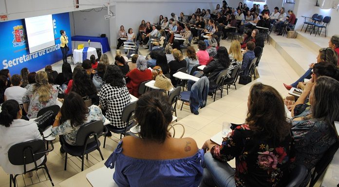 Pessoas vistas de costas assistindo uma palestra em um auditório