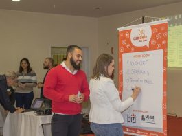 Mulher escreve lista em cartaz e homem olha enquanto ri