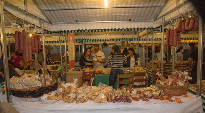 barracas de feira com diversos produtos embalados dispostos e ao fundo pessoas conversam com comerciante de costas