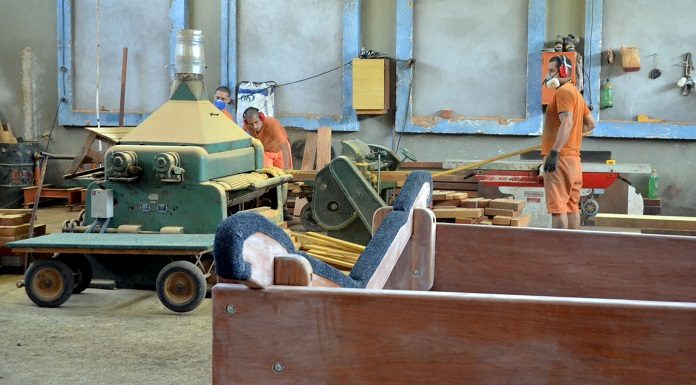 homens de uniforme laranja trabalhando em chão de fábrica, com diversos maquinários