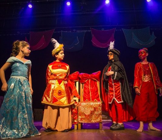 Apresentações das oficinas do Theatro Adolpho Mello iniciam em setembro quatro crianças usando vestes caricatas de árabes olham entre si sobre um palco com baixa iluminação