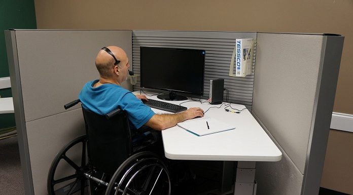 homem em cadeira de rodas trabalhando em um computador numa baia de escritório
