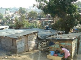 Desigualdade social contribui para o círculo vicioso da corrupção barracos de uma favela com algumas árvores; em primeiro plano, mulher negra se abaixa para lavar roupas