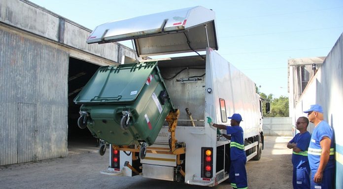 trabalhadores despejam grande conteiner em caminhão de lixo