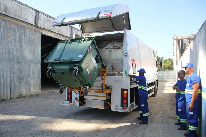 trabalhadores despejam grande conteiner em caminhão de lixo