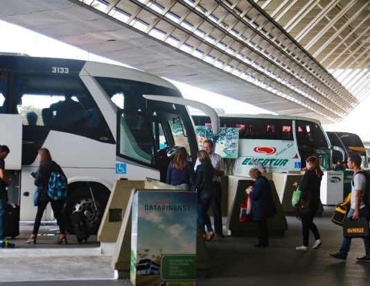 ônibus estacionados em rodoviária, com passageiros circulando na frente