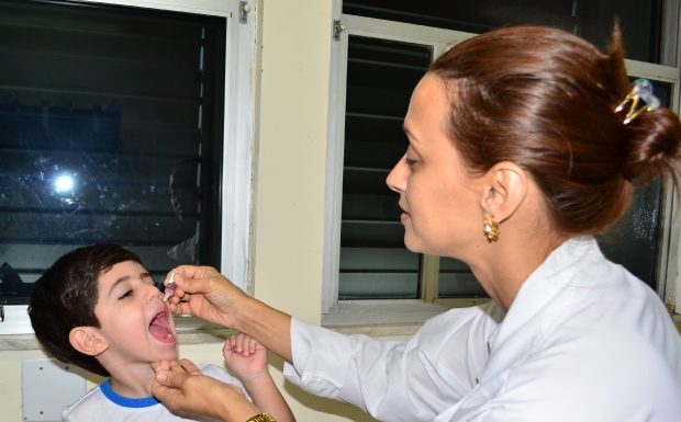 mulher usando traje de enfermeira despeja gotas na boca de um menino