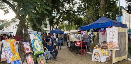 diversas barracas com produtos variados organizados em caminhos de pedras em praça arborizada